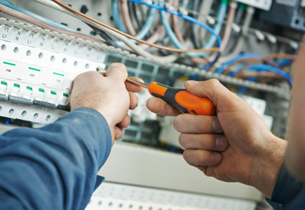 A close-up image of a hand holding pliers while working on an electrical panel