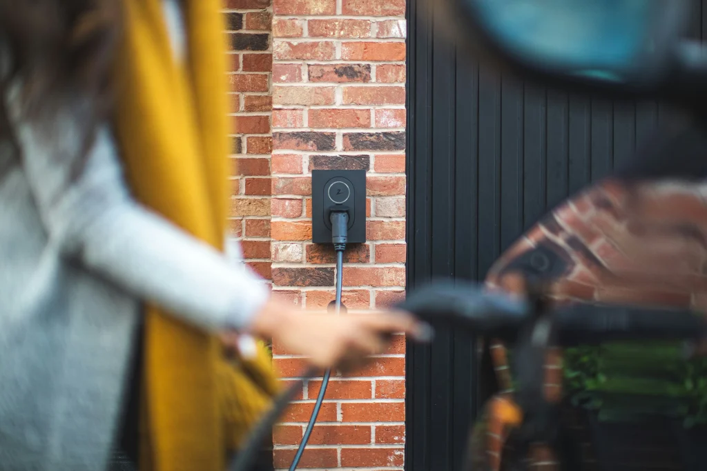 Lady pushing ev charger into car slot. View of EV charger installed on home wall.